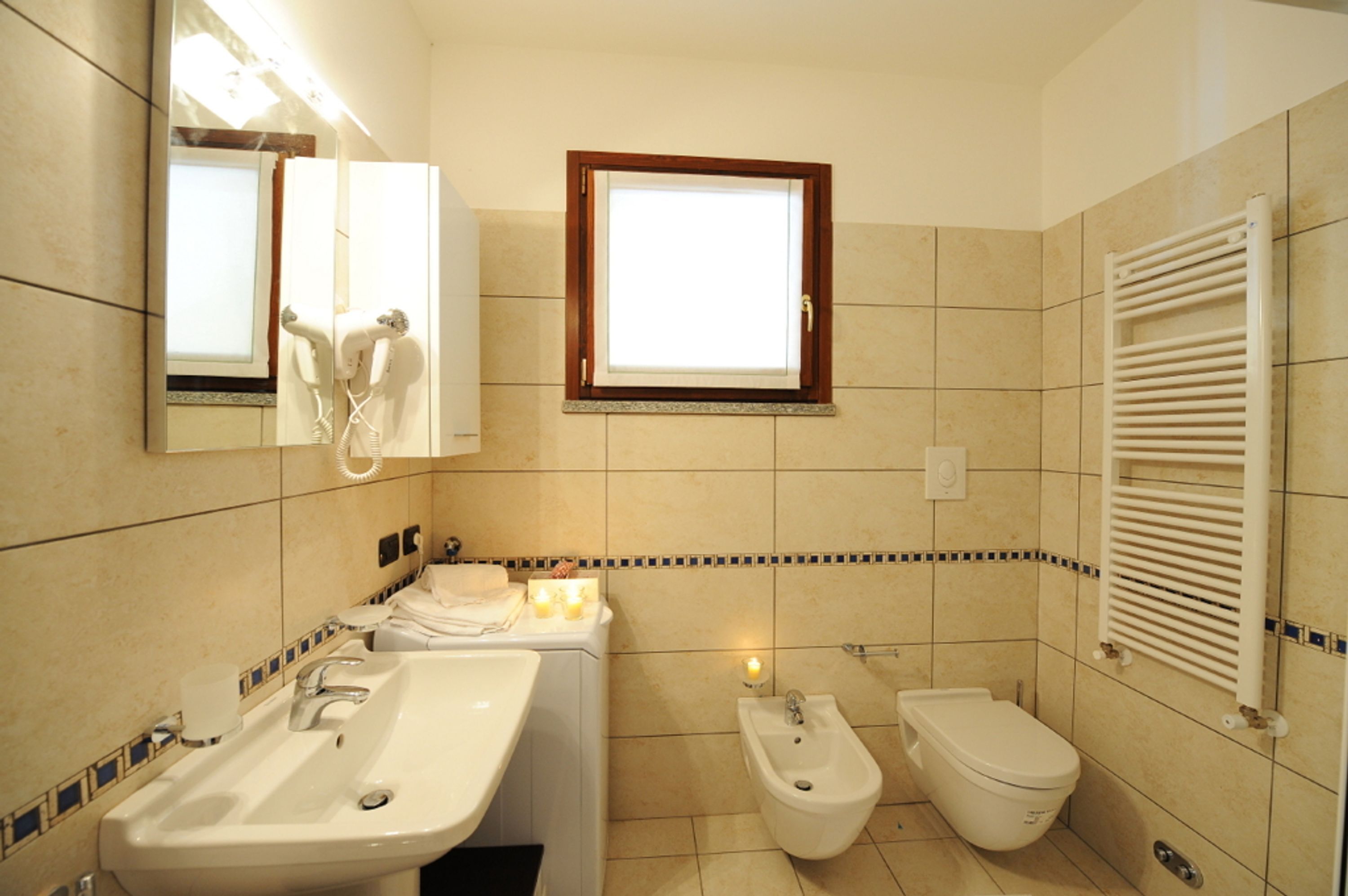 A bathroom with a sink, bidet, toilet, and a mirror with a hairdryer.