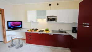 Une cuisine moderne avec des meubles rouges, un four à micro-ondes, une machine à café et un téléviseur posés sur un plan de travail blanc.