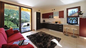 Eine moderne Küche mit einer großen Kochinsel, ein Essbereich mit einem roten Sofa und Blick auf eine gebirgige Landschaft durch große Schiebetüren.