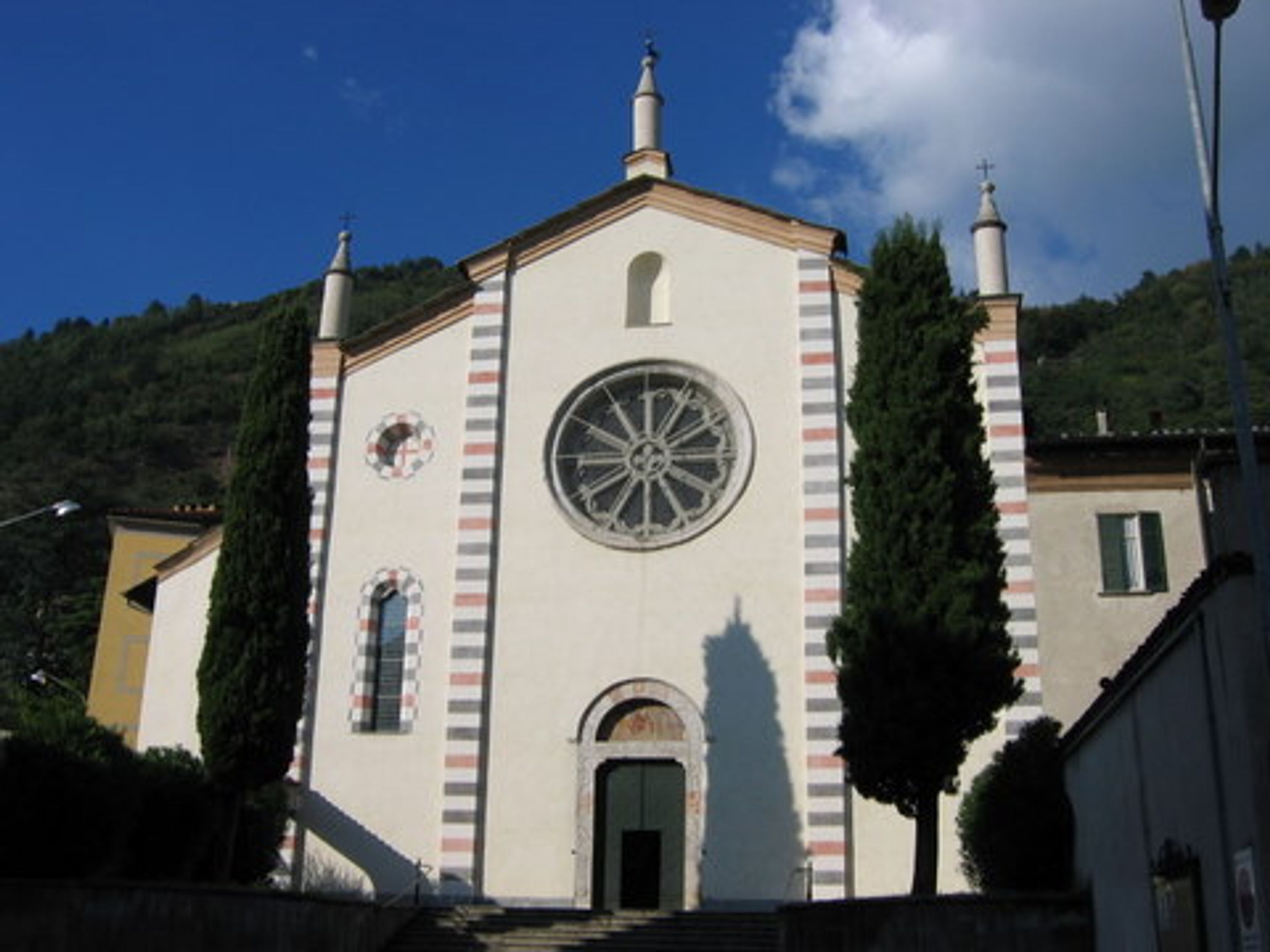 Una iglesia con una torre de campanario, una torre con campanas y un ventanal circular.