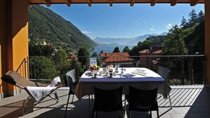 A terrace with a table set for two, overlooking a mountainous landscape with a lake. - Residence Eden Magnolia 17 (Argegno)