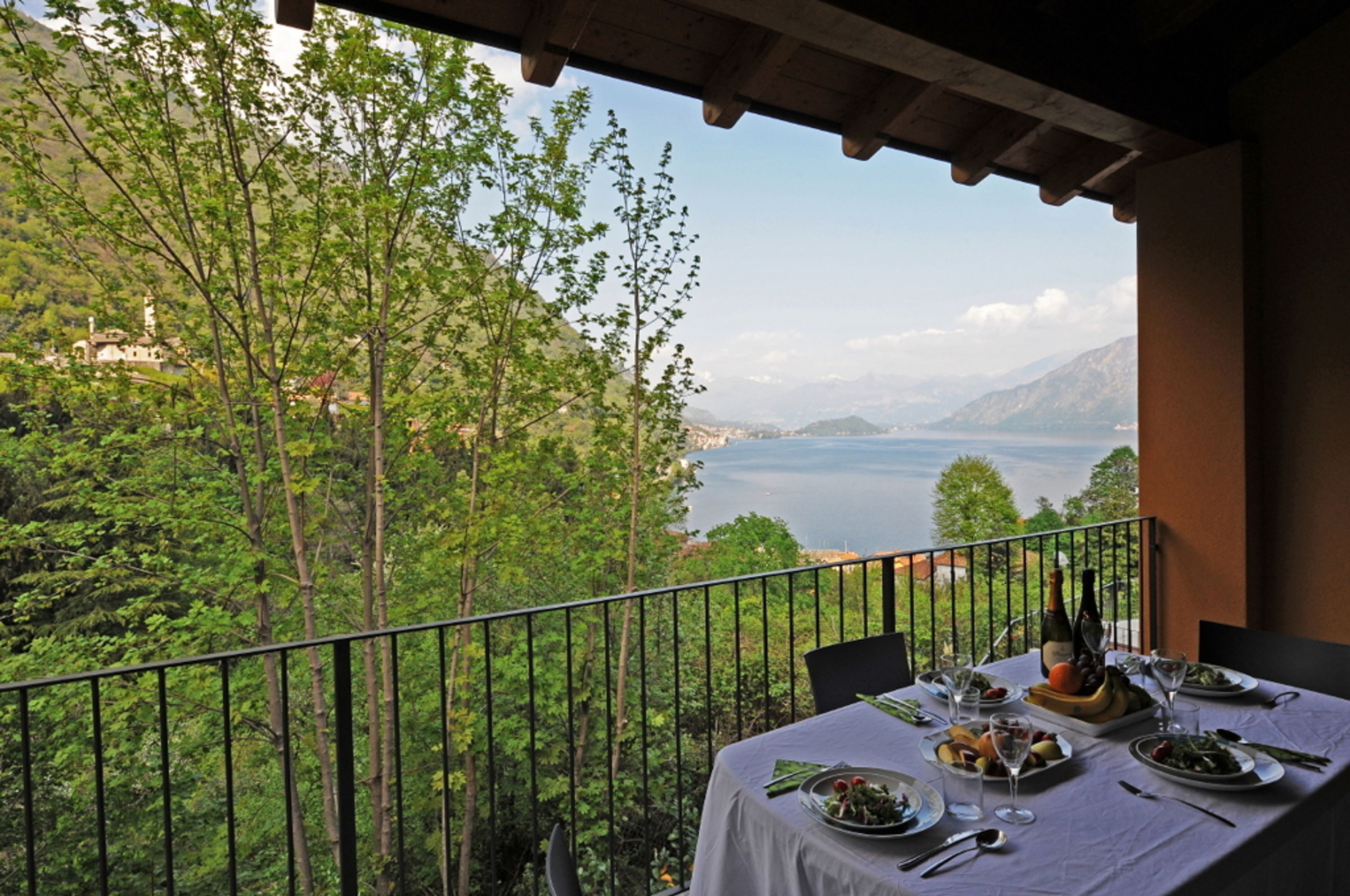A balcony with a table set for a meal, overlooking a mountainous landscape and a body of water.