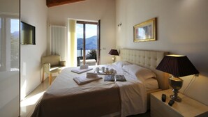 Un dormitorio con cama, mesita de noche, lámpara y vistas a montañas a través de una puerta abierta.