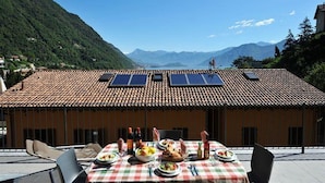Un coin repas avec une table dressée pour le repas, des panneaux solaires sur le toit et une chaîne de montagnes en arrière-plan.
