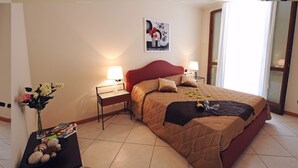 Une chambre à coucher bien rangée, avec un grand lit, des lampes de chevet, une petite table sur laquelle est posé un vase de fleurs et un tableau encadré au mur.
