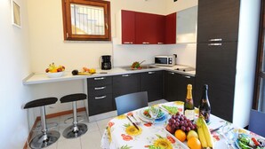 A compact kitchen with a microwave, red cabinets, and a dining area with a table set for two. - Residence Eden Magnolia 15 (Argegno)