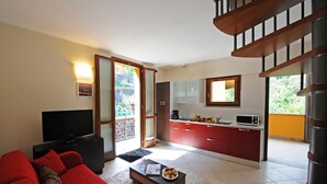 Una sala de estar moderna con un sofá rojo, un televisor de pantalla plana y una zona de comedor con armarios rojos y un microondas.