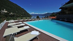 Piscina con sillas de descanso y vistas a un lago y montañas.