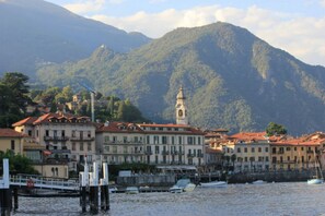 A coastal town with buildings, a dock, and a mountain in the background. - Villa Aurelia in Plesio (Plesio)