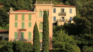 A two-story building with a red roof and green shutters, surrounded by dense trees. - Villa Aurelia in Plesio (Plesio)