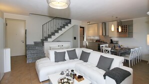 A modern living room with a white sofa, grey cushions, a coffee table with drinks, a staircase, and a kitchen area. - Villa Aurelia in Plesio (Plesio)