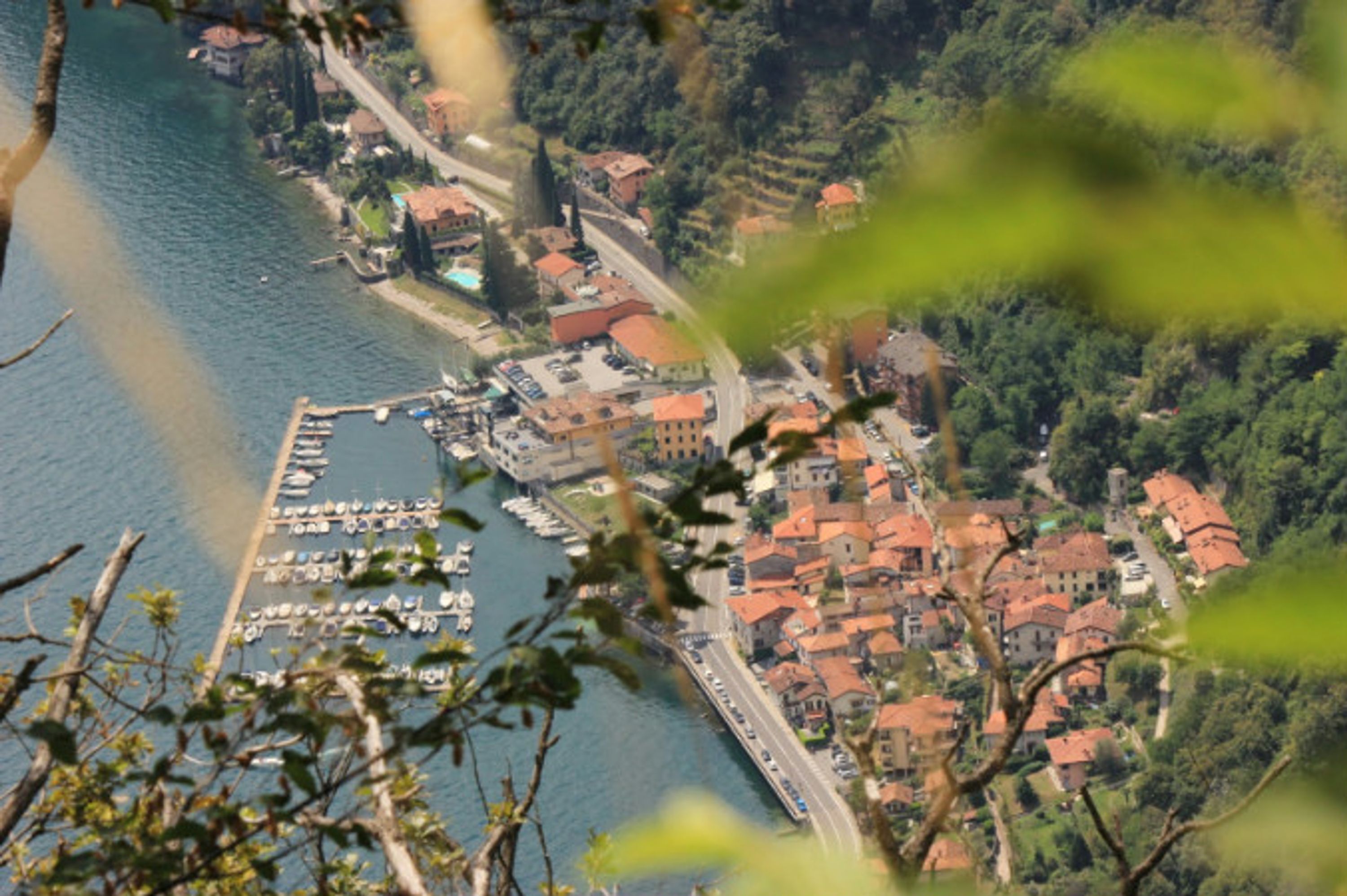 Vista aérea de un pueblo costero con un puerto deportivo, edificios de tejados rojos y abundante vegetación.