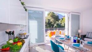 A modern kitchen with a dining area, a balcony with outdoor furniture, and a view of trees and mountains. - Casa Laura Apt 6 in Il Piazzo (Plesio)