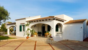 Un bâtiment blanc avec un toit en tuiles, une véranda abritée avec des chaises et un garage.