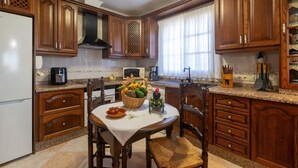 A kitchen with wooden cabinets, a granite countertop, a dining table with chairs, and a window with curtains. - El Descanso in Mijas (Mijas)