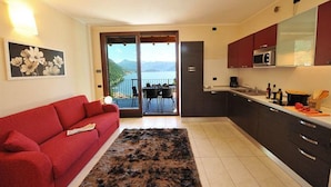 Una cucina moderna con mobili scuri, un divano rosso e vista mare tramite una porta scorrevole.