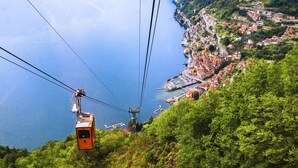 Una funivia che si muove sopra una rigogliosa collina verde, con vista su una località costiera sottostante.
