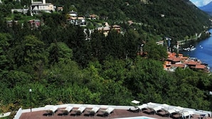 Una piscina con lettini, circondata da un pontile in legno, con montagne sullo sfondo e vista sul mare.