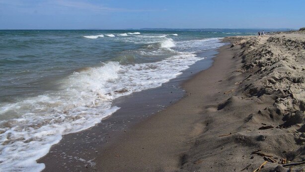 Ein sandiger Strand mit brechenden Wellen und blauem Himmel.