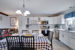 Une cuisine moderne avec des meubles blancs, une table à manger pour quatre personnes et un lustre.