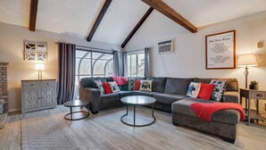 Ein modernes Wohnzimmer mit einer Eckcouch, zwei runden Couchtischen, einem Kamin und großen Fenstern.