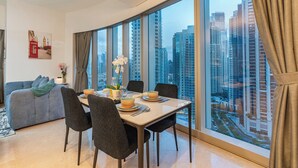 A dining area with a table set for two, a sofa, and a large window with a city view. - Iconic Views -Burj Khalifa & Fountain Views (Dubai)