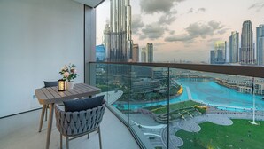A balcony with a table and chairs, overlooking a cityscape with high-rise buildings and a waterfront area. - Iconic Views -Burj Khalifa & Fountain Views (Dubai)