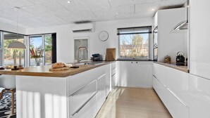 A modern kitchen with white cabinetry, a wooden countertop, a built-in oven, and a window providing natural light. - Beautiful home in Glesborg (Glesborg)
