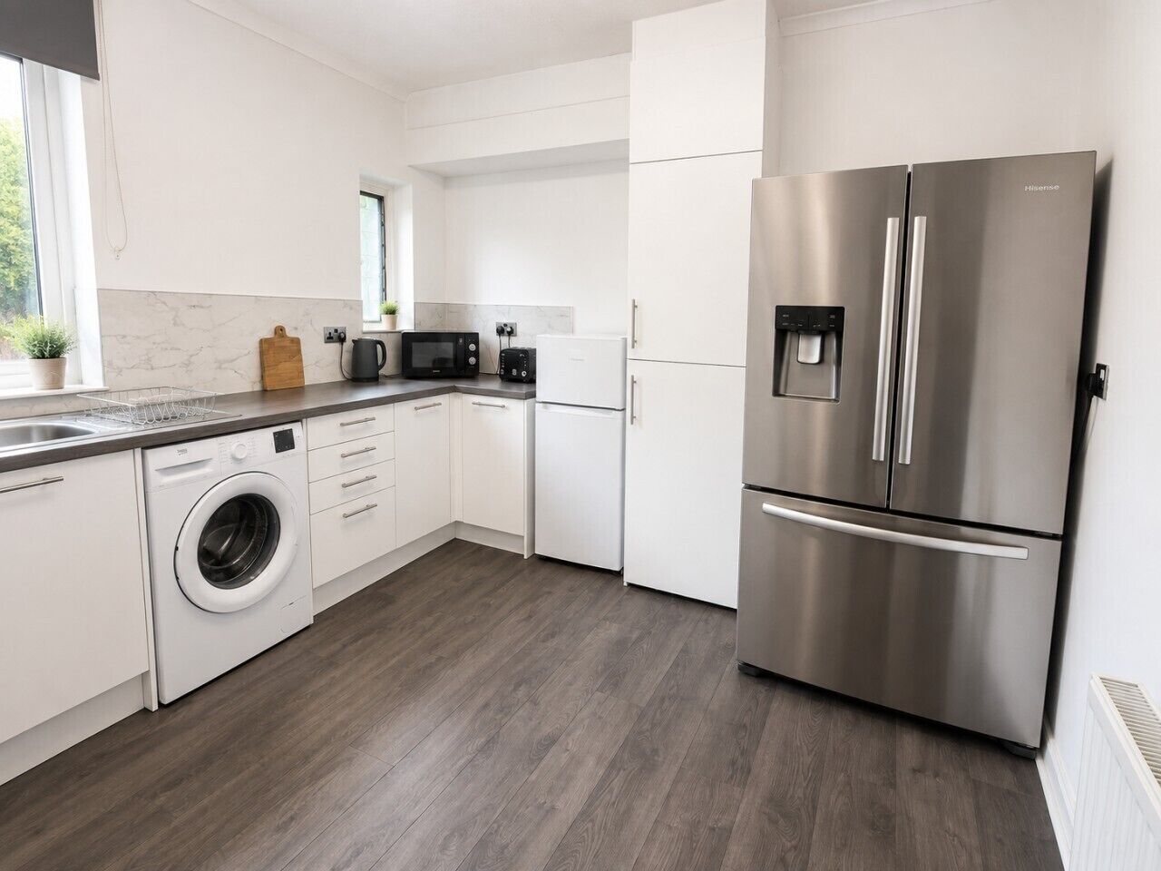 A modern kitchen with a stainless steel refrigerator, a washing machine, and a microwave.