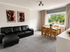 Ein Wohnzimmer mit einer schwarzen Ledersofa, einem Esstisch mit Stühlen und zwei abstrakten Gemälden an der Wand.