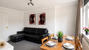 A modern living room with a black leather sofa, a dining table set with plates and glasses, and two abstract paintings on the wall.