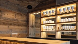 A wooden interior with a central counter and shelves displaying glassware. - Alta Rocca, 14-guest chalet in Gérardmer – pool, jacuzzi, sauna (Gérardmer)