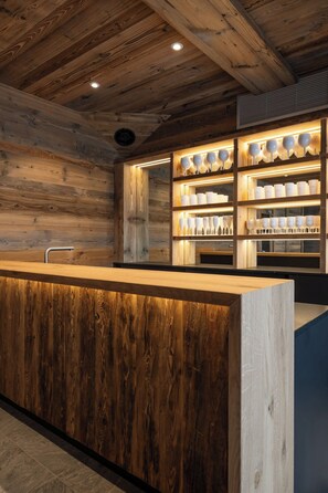 A wooden interior with a central counter and shelves displaying glassware. - Alta Rocca, 14-guest chalet in Gérardmer – pool, jacuzzi, sauna (Gérardmer)