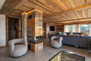 A modern living room with a stone fireplace, a sofa set, and a glass coffee table. - Alta Rocca, 14-guest chalet in Gérardmer – pool, jacuzzi, sauna (Gérardmer)