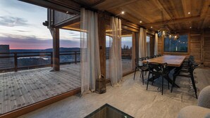 A spacious room with a large wooden table and chairs, large windows with curtains, and a view of the landscape. - Alta Rocca, 14-guest chalet in Gérardmer – pool, jacuzzi, sauna (Gérardmer)