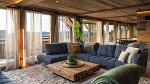 A spacious living area with a large sofa, a coffee table, and a dining table. - Alta Rocca, 14-guest chalet in Gérardmer – pool, jacuzzi, sauna (Gérardmer)