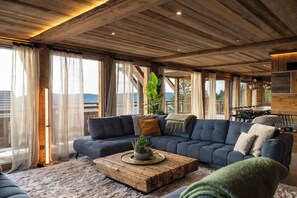 A spacious living area with a large sofa, a coffee table, and a dining table. - Alta Rocca, 14-guest chalet in Gérardmer – pool, jacuzzi, sauna (Gérardmer)