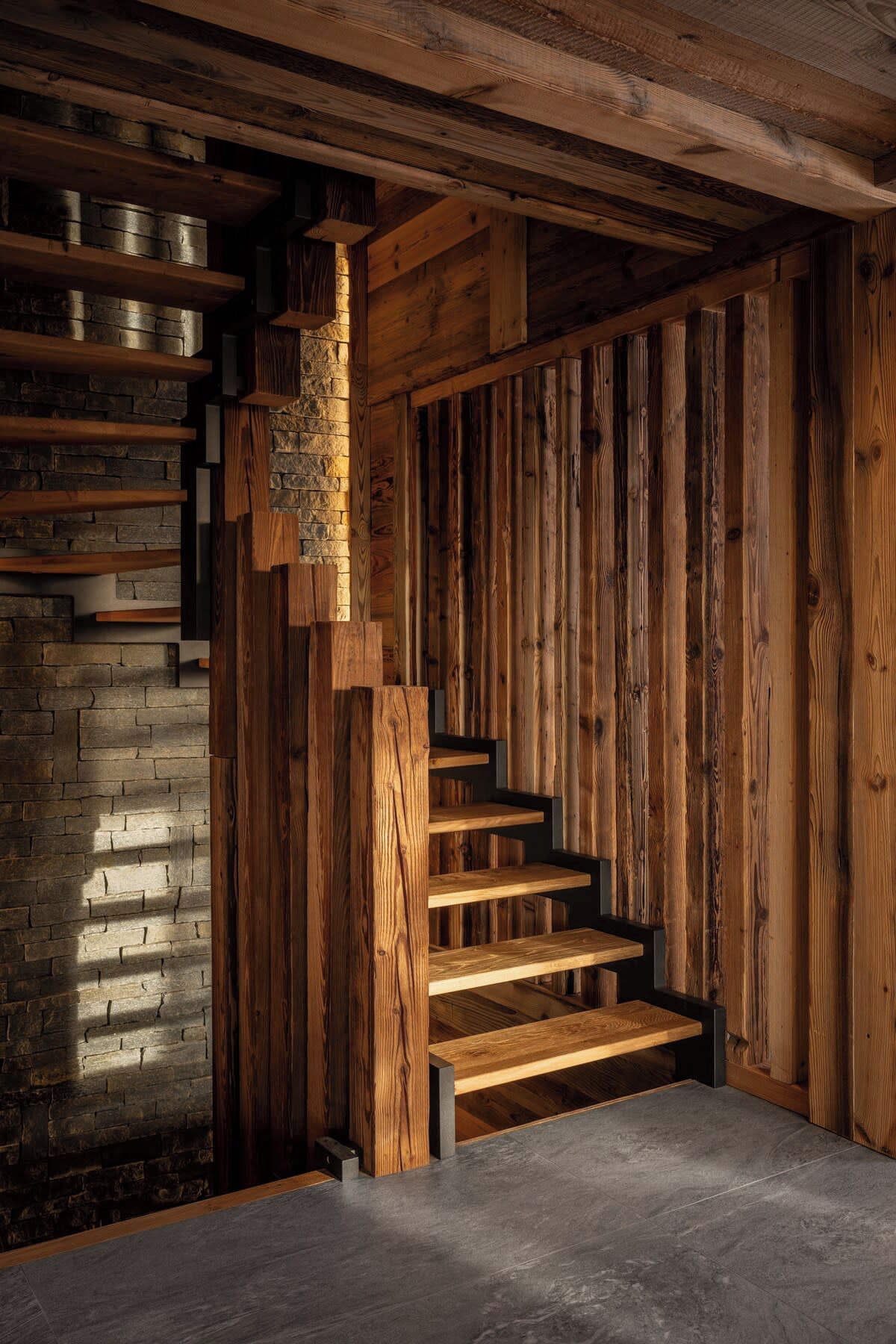 A wooden staircase with a stone wall on one side and a wooden panel wall on the other.