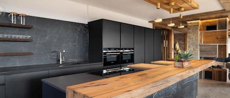 A modern kitchen with a central island, black cabinetry, and a wooden countertop.
