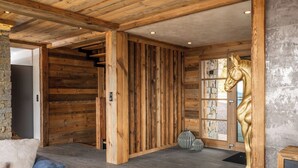 A wooden interior with a stone wall, a large wooden door, and a golden horse statue. - Alta Rocca, 14-guest chalet in Gérardmer – pool, jacuzzi, sauna (Gérardmer)