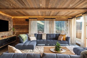 A modern living room with a sectional sofa, a flat-screen TV, and a wooden ceiling. - Alta Rocca, 14-guest chalet in Gérardmer – pool, jacuzzi, sauna (Gérardmer)