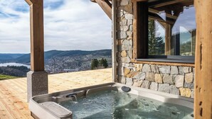 A hot tub with a stone wall and wooden beams, overlooking a mountainous landscape. - Alta Rocca, 14-guest chalet in Gérardmer – pool, jacuzzi, sauna (Gérardmer)
