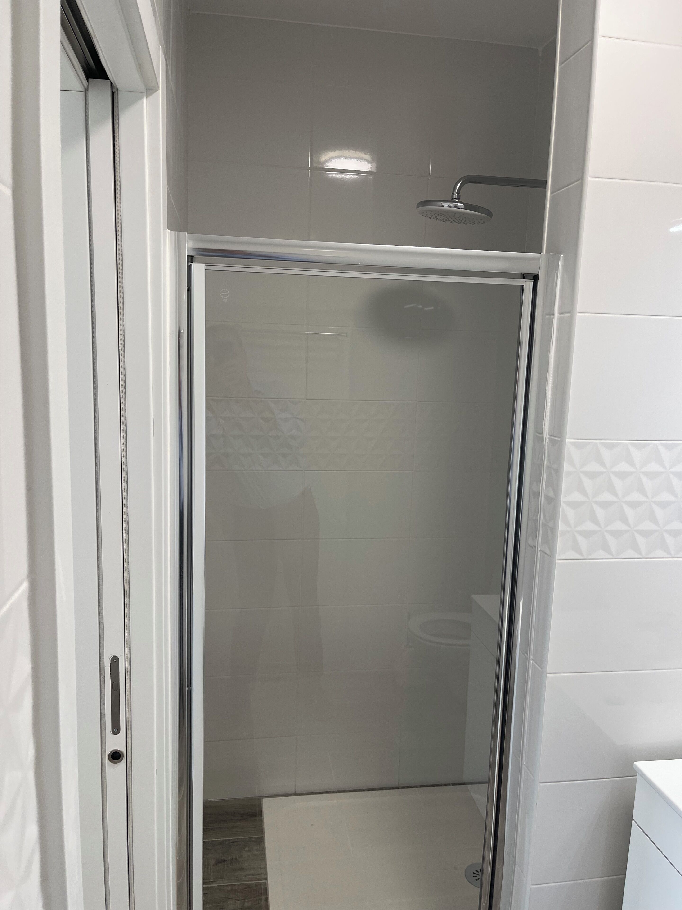 Ein modernes Badezimmer mit einer Duschkabine aus Glas, weißen Fliesenwänden und einer sichtbaren Toilette.
