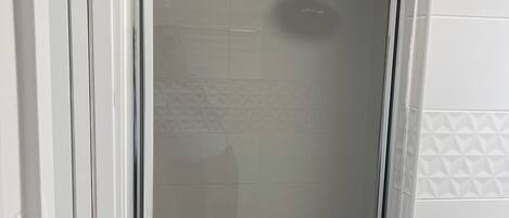 Ein modernes Badezimmer mit einer Duschkabine aus Glas, weißen Fliesenwänden und einer sichtbaren Toilette.