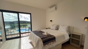 Une chambre à coucher comprenant un lit, une table de chevet, une commode, une fenêtre donnant sur une piscine et un espace verdoyant, ainsi qu’un appareil de climatisation.