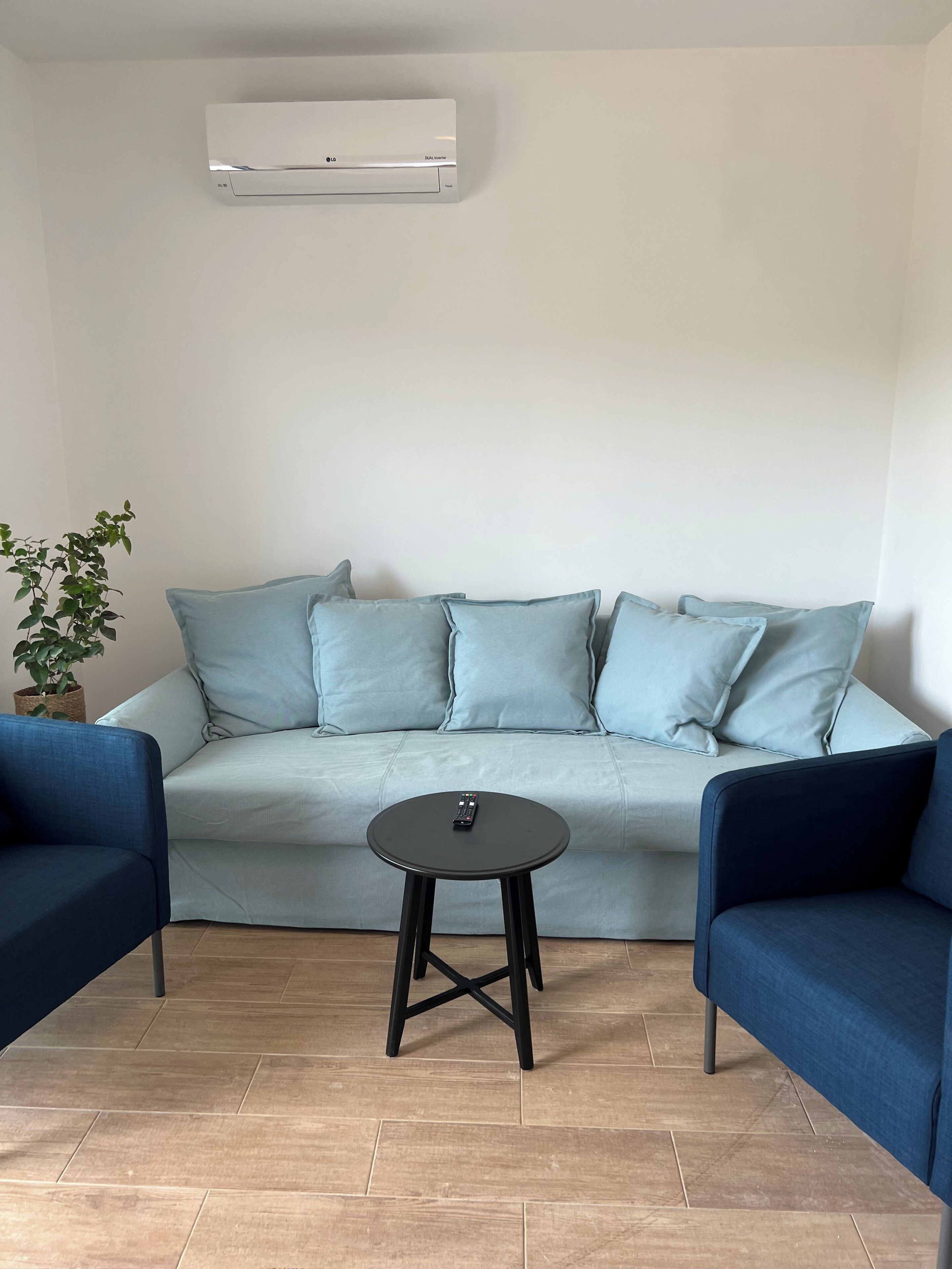 Un salon moderne avec un canapé bleu clair, deux fauteuils bleu foncé, une petite table ronde et une plante en pot.
