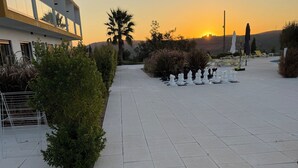 Un espace extérieur aménagé avec une surface pavée, un jeu d’échecs, des chaises longues et un bâtiment doté de balcons.