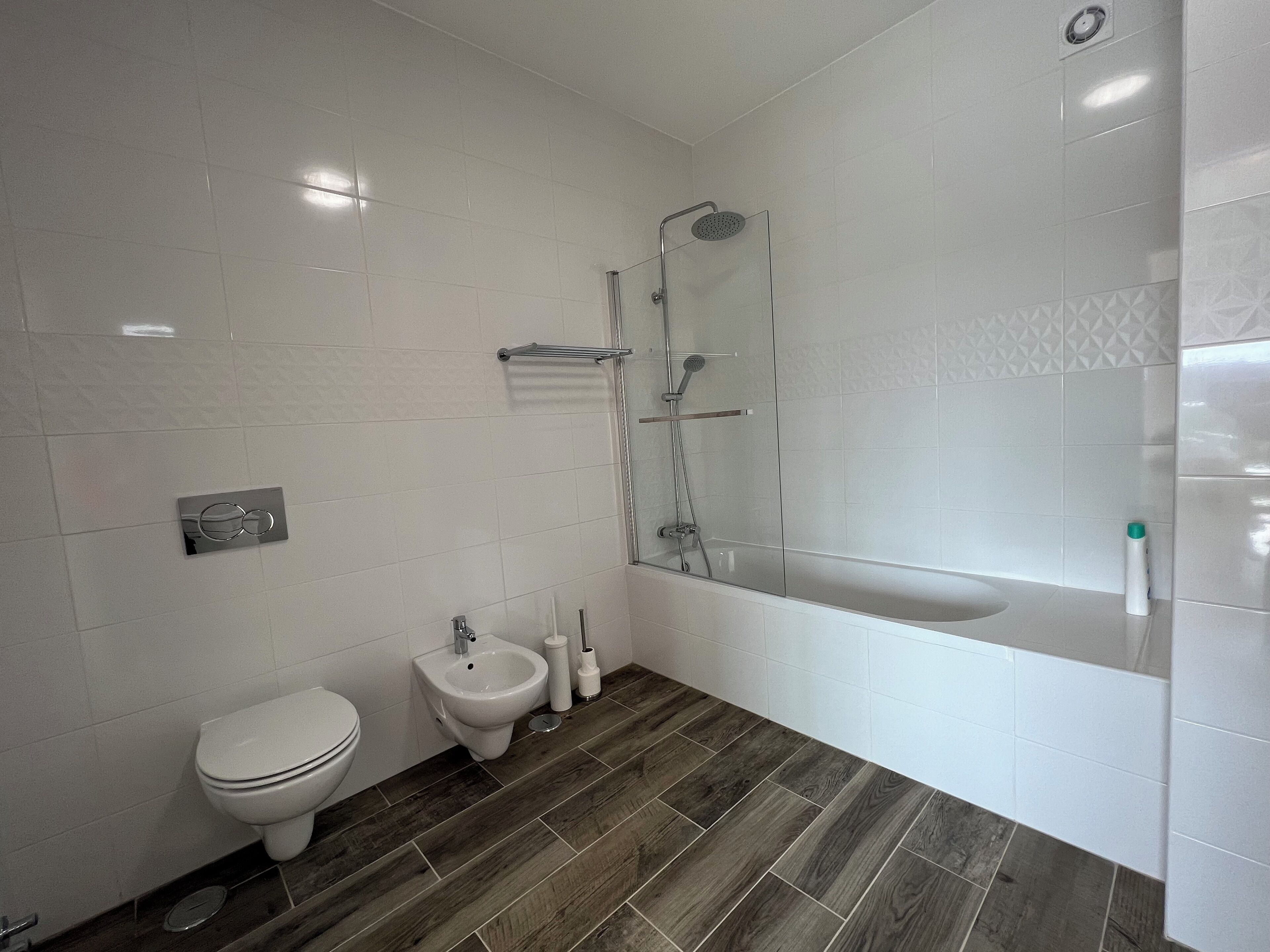 Een moderne badkamer met toilet, bidet en een douchecabine met glazen wanden.