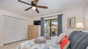 A bedroom with a bed, a ceiling fan, a wardrobe, a TV, and a view of the outside. - Beachy Retreat 1 Mile to Beach (Satellite Beach)