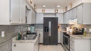 A modern kitchen with white cabinets, a stainless steel refrigerator, a built-in oven, and a granite countertop. - Beachy Retreat 1 Mile to Beach (Satellite Beach)